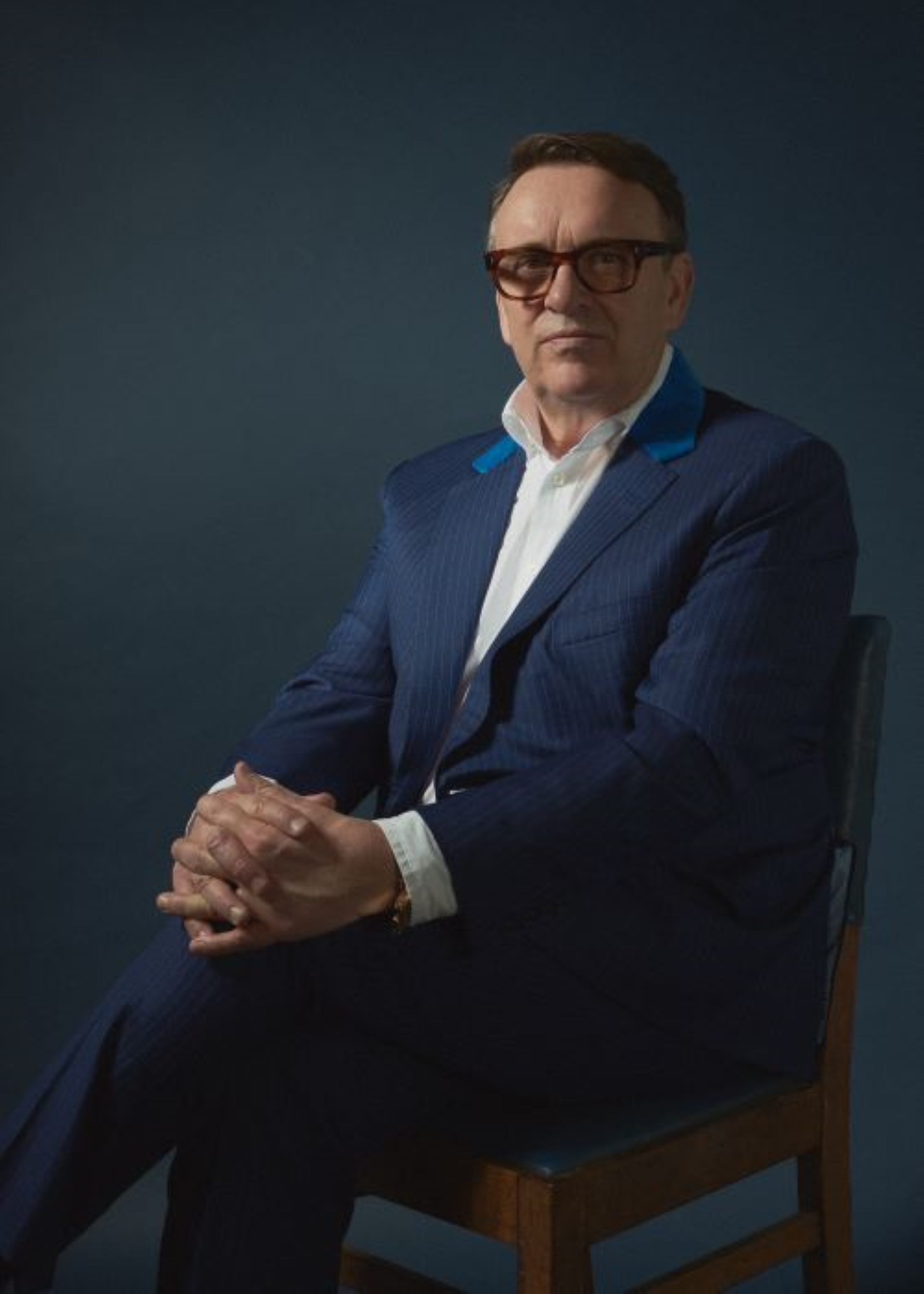 Chris Difford sitting on a chair in a blue suit