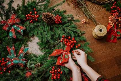 A pair of hands tying a red bow onto a Christmas wreath