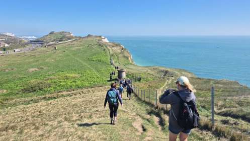 A group of people walking along a clifftop with sea to the side