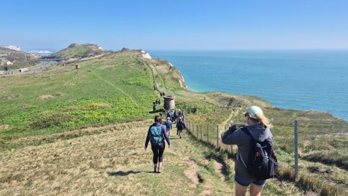 A group of people walking along a clifftop with sea to the side