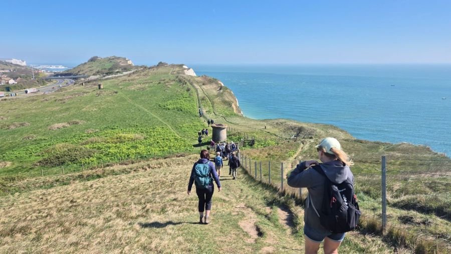 A group of people walking along a clifftop with sea to the side