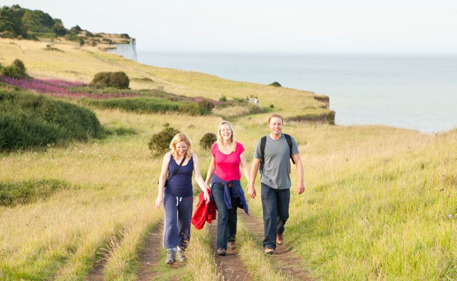 Three people walking on the path near the cliff edge with the sea in the background.