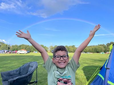 A smiling boy on a campsite with his arms in the air