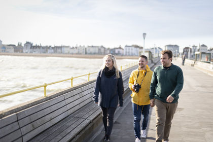 Three people walking on Deal Pier towards the camera with the seafront in the background.