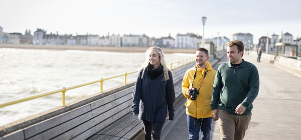 Three people walking on Deal Pier towards the camera with the seafront in the background.