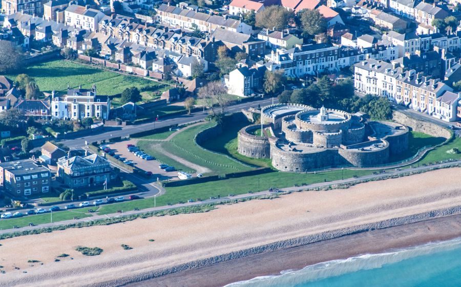 A Tudor castle from the air with beach and houses around.