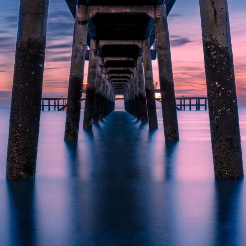 Deal Pier from below with pink and purple sea and sky.