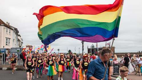 Deal Pride parade with rainbow flags held aloft