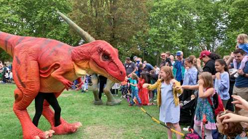 A large red dinosaur puppet and a crowd of children
