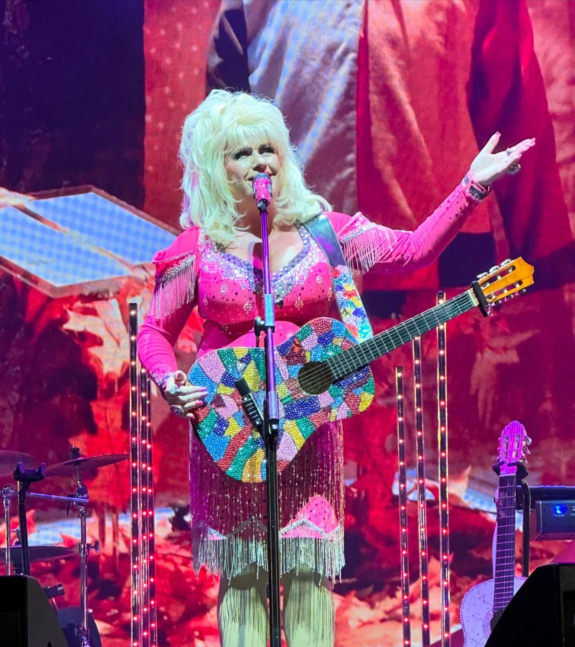 Sarah performing on stage as Dolly Parton with her multi-coloured sequin covered guitar