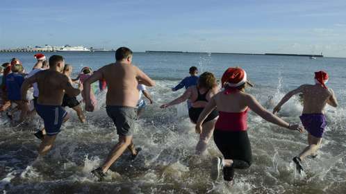 A group of people in swimwear run into the sea next to Dover ferry port