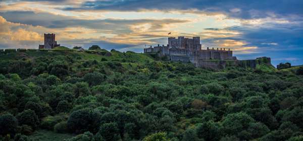 A dark sky over Dover Castle with green trees in the foreground