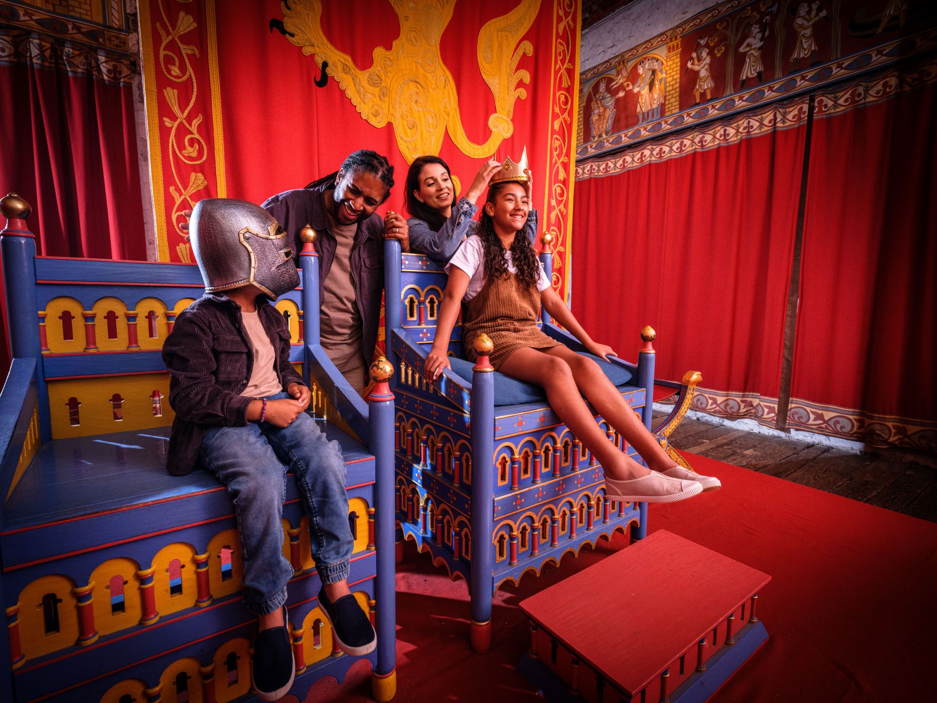 Two children sitting on blue and gold thrones, their parents standing behind