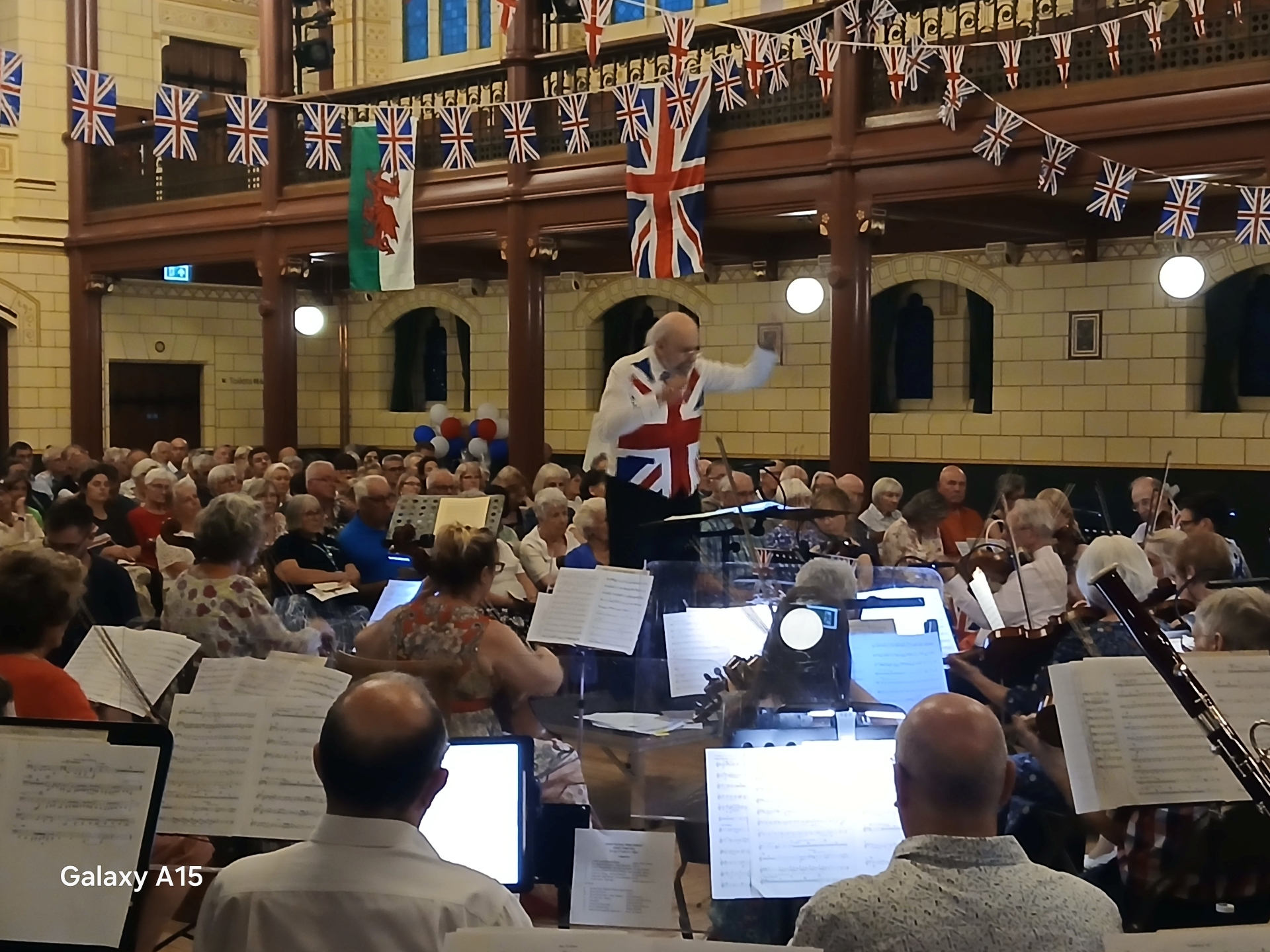 A man in a union jack waistcoat conducting an orchestra