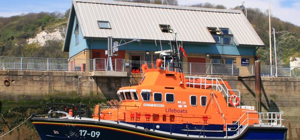 An orange and navy lifeboat in Dover Harbour in front of the Lifeboat station