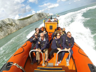 A large orange inflatable boat with passengers wearing life jackets whizzing through the sea beside the White Cliffs of Dover