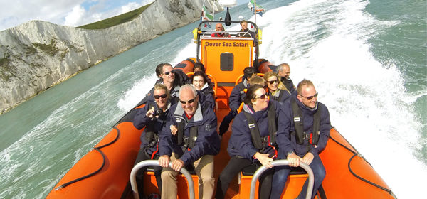A large orange inflatable boat with passengers wearing life jackets whizzing through the sea beside the White Cliffs of Dover