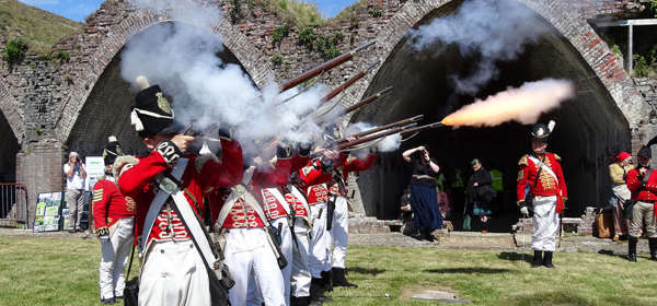 Re-enactors dressed as Napoleonic soldiers firing weapons. 