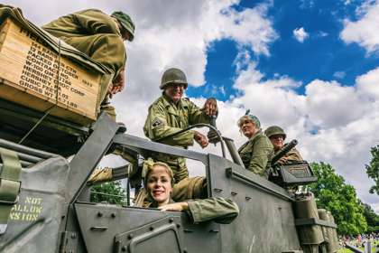 A group of people in army fatigues in a jeep with blue sky behind.