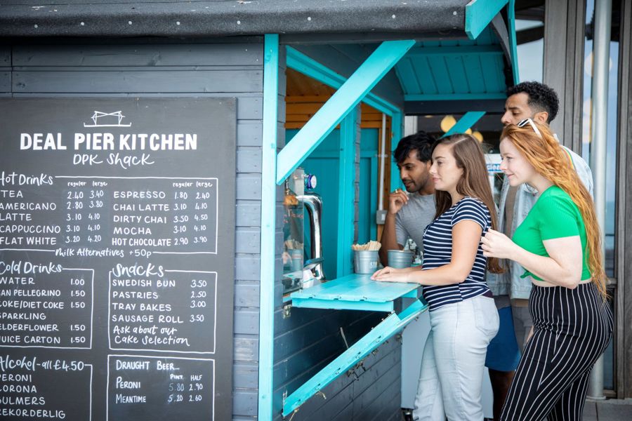A chalkboard with menu next to a hatch with a queue of people being served