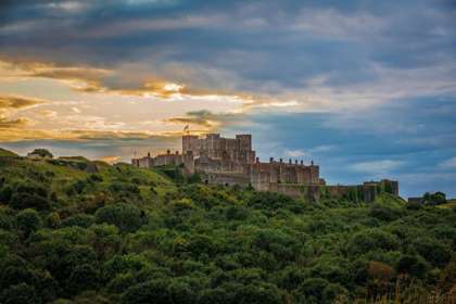 Dover Castle from a distance in the early morning light with a pink sky and greenery in the foreground.