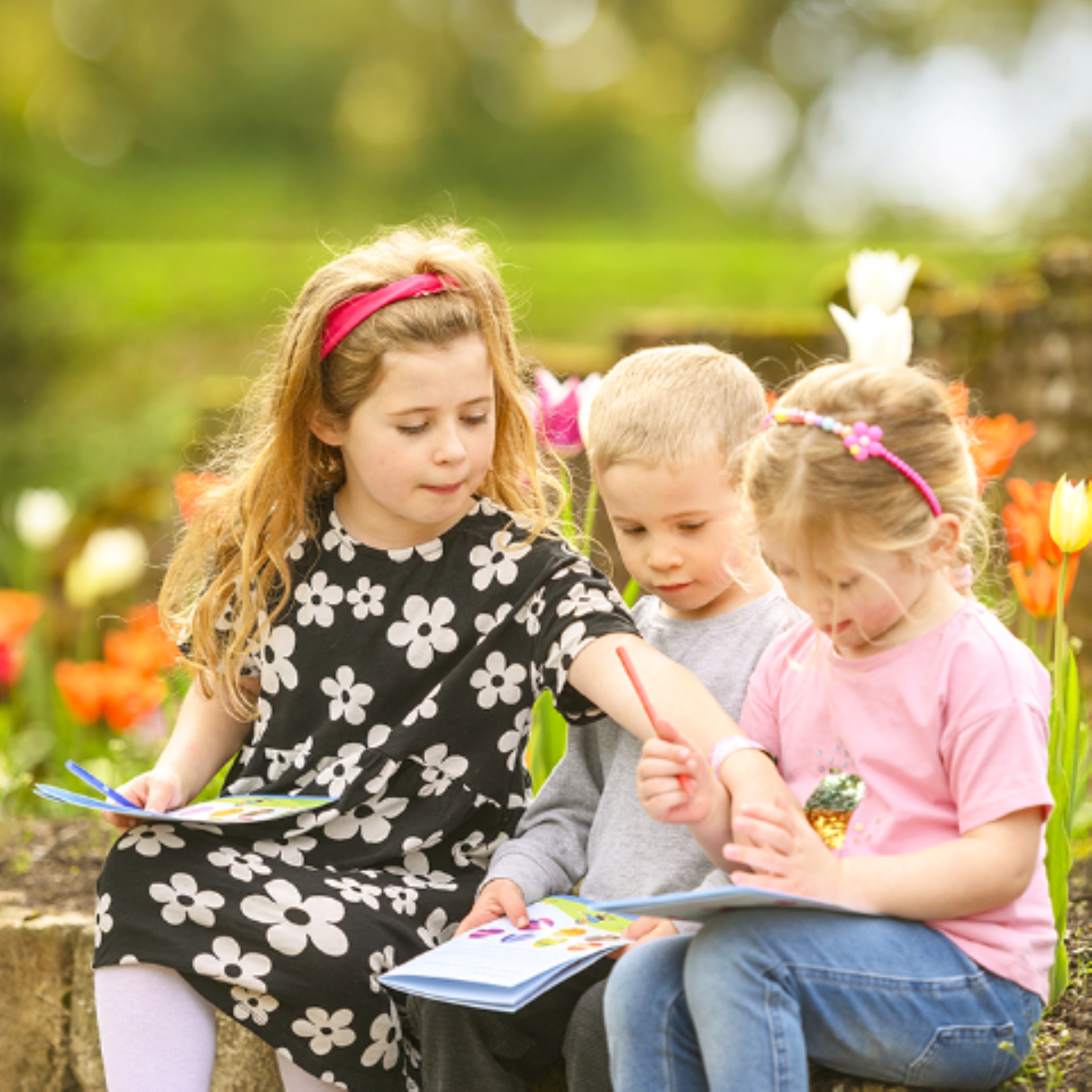 3 children sitting on a wall looking at quest leaflet