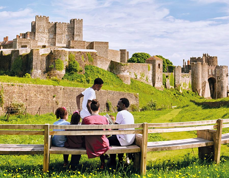 A family of five sitting on a wooden bench with Dover Castle in the background