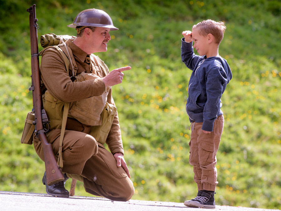 A soldier kneeling and a small boy saluting him.