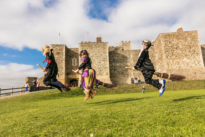 Three children on broomsticks in front of Dover Castle