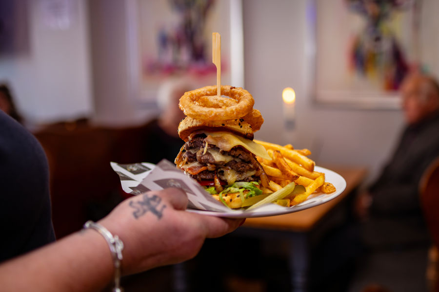 Burger and chips with onion rings being served on a plate