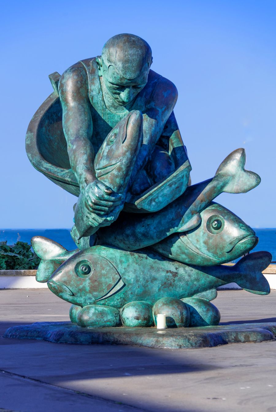 Bronze sculpture of a fisherman in a boat catching large fish.