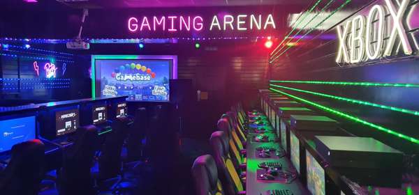 A row of gaming chairs, screens and equipment inside a gaming arena with neon lights on the walls
