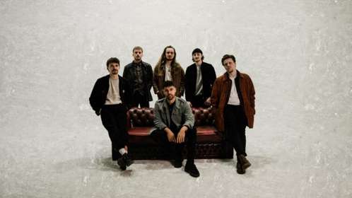 band members sitting and standing around a leather couch
