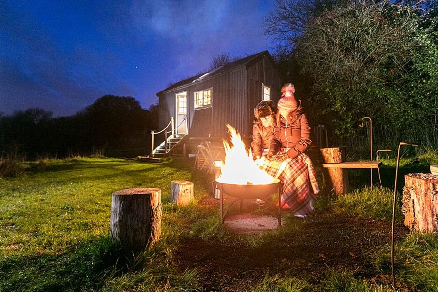 Couple sitting outside Shepherd's Hut at night with lit fire pit