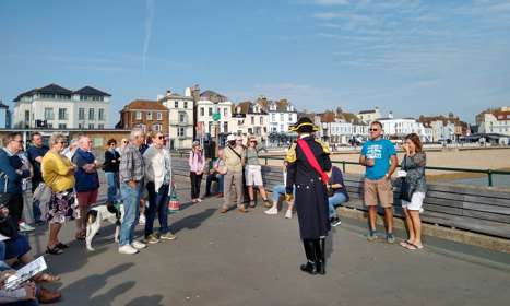 A man dressed in Napoleonic costume talking to a group of tourists on Deal Pier with the beach and seafront in the background.