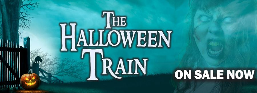 A glowing spooky pumpkin face next to a gate with a black cat sitting on a fence close by, The Halloween Train
