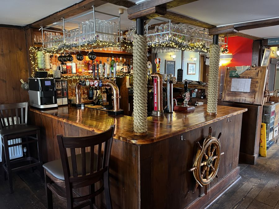 A pub bar interior with nautical theme - rope coiled around columns and ship's wheel on the side.