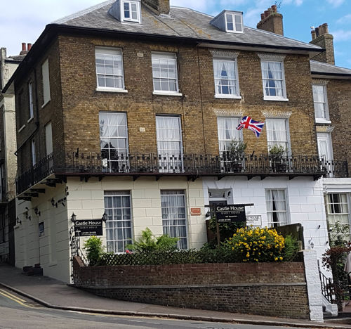 A large, period brick building with a wrought iron balustrade and period windows on a corner.