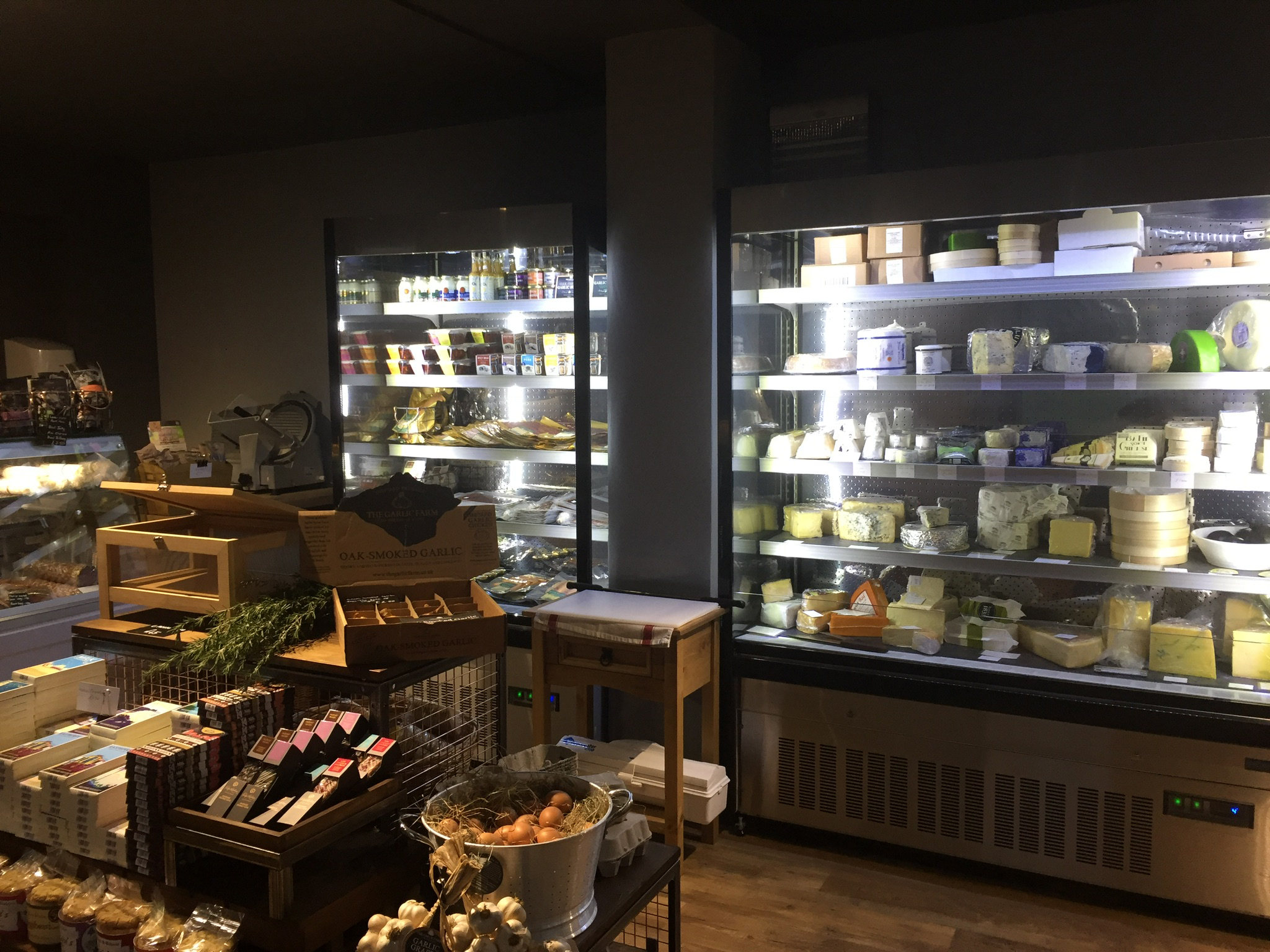 Interior of a delicatessen with fridge full of cheeses and a display of other foods.