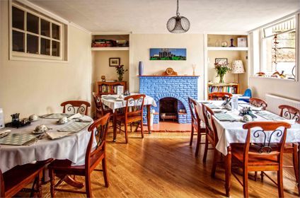 A dining room with three tables and chairs laid with tablecloths and crockery for breakfast.