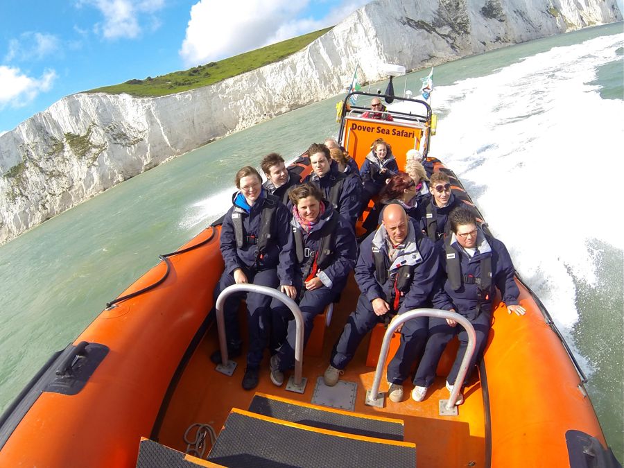 A group of people wearing lifejackets aboard an orange inflatable speedboat whizzing past the White Cliffs.