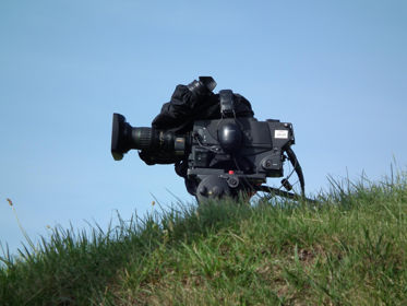 Film camera sitting on grass with blue sky behind.