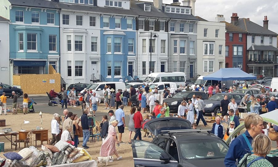 Stalls and cars with crowds of people and a row of houses behind