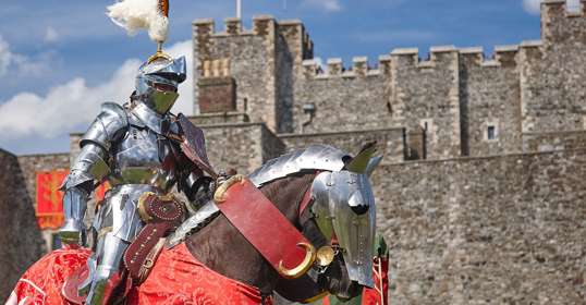 A knight in armour sits on his horse in front of the medieval Great Tower at Dover Castle