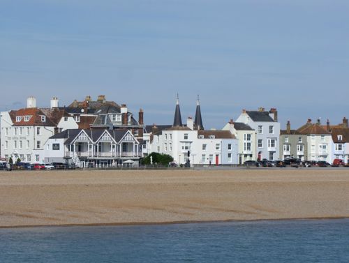 A row of white and pastel coloured buildings with a shingle beach and sea in the foreground.