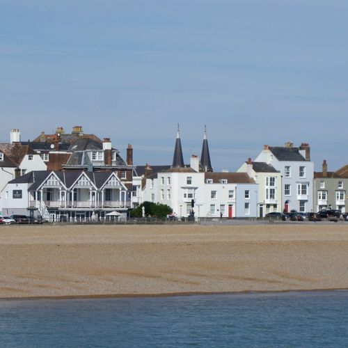 A row of white and pastel coloured buildings with a shingle beach and sea in the foreground.