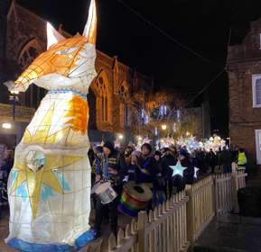 A large fox lantern at the head of a procession of smaller star lanterns and drummers