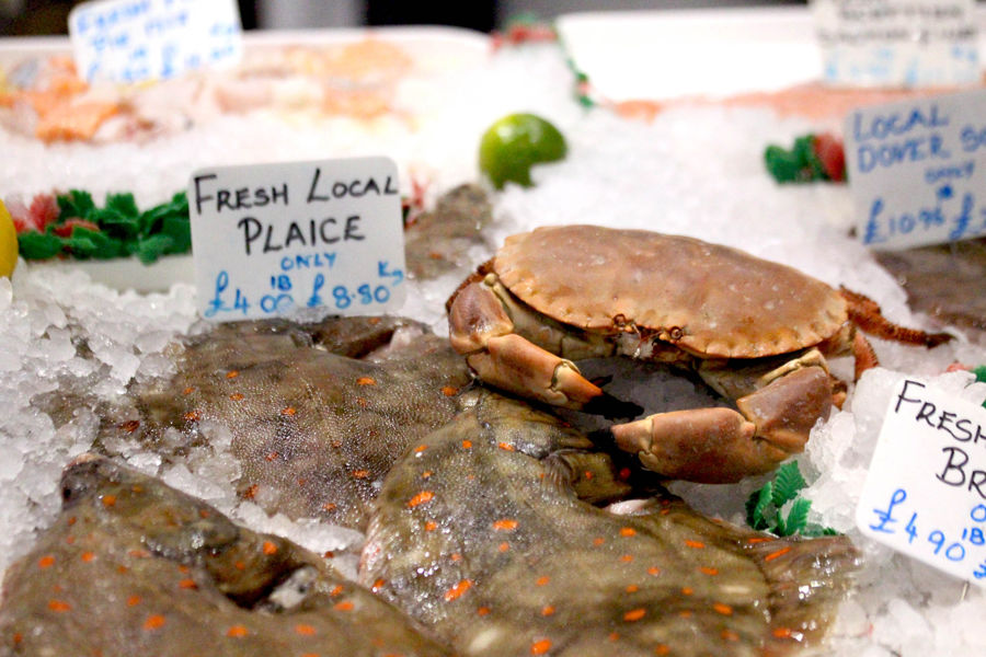 A display of fresh fish including plaice and crab on ice with pricing labels.