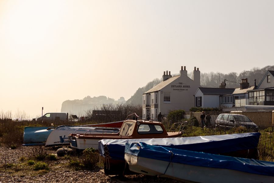 Boats on a shingle beach with The Zetland Arms pub in the background.