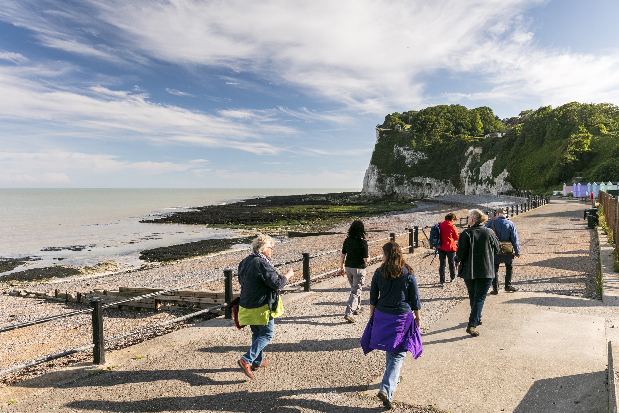 A group of walkers beside a beach with cliffs in the background.